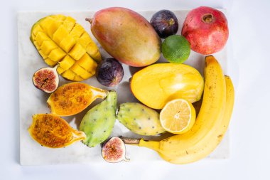 Mermer tahtada taze tropik egzotik meyve tabağı: mango, pitaya, limon, limon, muz, incir.