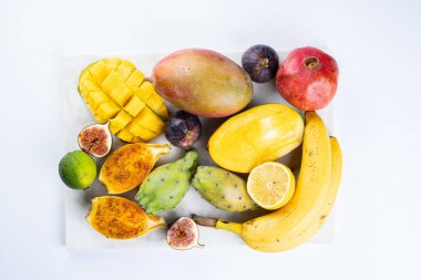 Mermer tahtada taze tropik egzotik meyve tabağı: mango, pitaya, limon, limon, muz, incir.