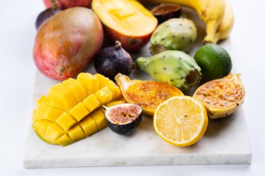 Mermer tahtada taze tropik egzotik meyve tabağı: mango, pitaya, limon, limon, muz, incir.