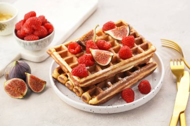 Taze ev yapımı Belçika waffle 'ı, ballı pudra şekeri, taze ahududu ve beyaz tabakta incir.