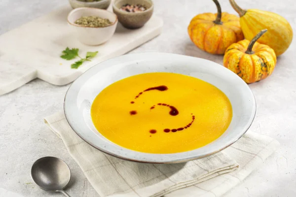 One deep grey soup bowl with an orange pumpkin cream soup with pumpkin seed oil, on a gray concrete background