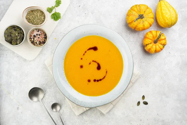 One deep grey soup bowl with an orange pumpkin cream soup with pumpkin seed oil, on a gray concrete background, top view
