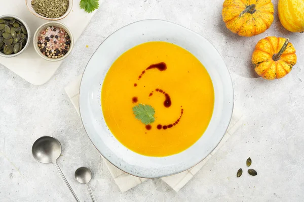 One deep grey soup bowl with an orange pumpkin cream soup with pumpkin seed oil, on a gray concrete background, top view
