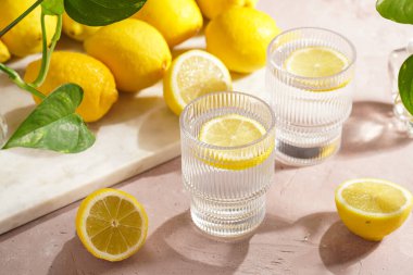 Sabah içeceği - iki bardak limon suyu ve taze narenciye dilimleri, soluk pembe arka planda bir sürü limon.