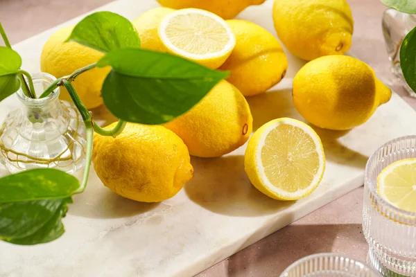 朝の飲み物 新鮮な柑橘類のスライスとレモン水の2つのガラス 淡いピンクの背景に多くのレモン全体 — ストック写真