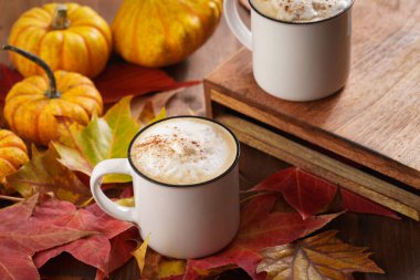 Kırmızı, sarı ve turuncu yapraklı, ahşap zemin üzerinde hokkaido balkabaklı, sade kahve ve beyaz süt köpüklü ve tarçın baharatlı bir sonbahar ortamı.