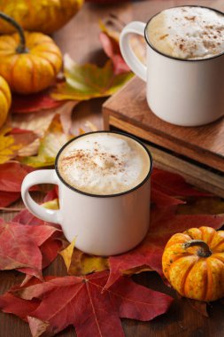Kırmızı, sarı ve turuncu yapraklı, ahşap zemin üzerinde hokkaido balkabaklı, sade kahve ve beyaz süt köpüklü ve tarçın baharatlı bir sonbahar ortamı.