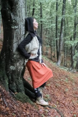 a woman stands near a tree in the forest