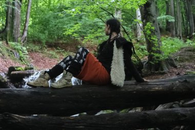 a woman sits on a log near a stream in the forest