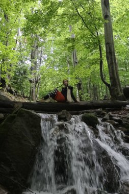 a woman sits on a log near a stream in the forest