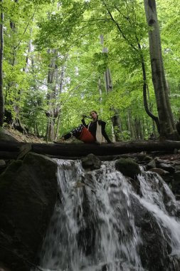a woman sits on a log near a stream in the forest