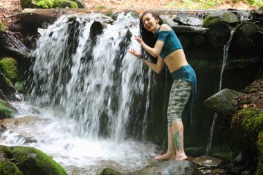Esmer kadın dağ şelalesinin yanında poz veriyor, Karpatya ormanı, yaz tatili.