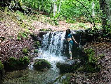 Esmer kadın dağ şelalesinin yanında poz veriyor, Karpatya ormanı, yaz tatili.