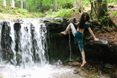 Esmer kadın dağ şelalesinin yanında poz veriyor, Karpatya ormanı, yaz tatili.