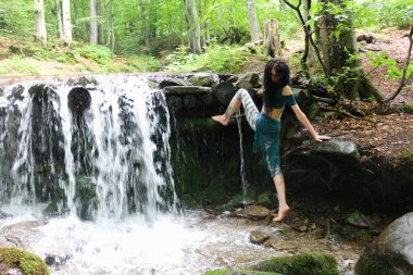 Esmer kadın dağ şelalesinin yanında poz veriyor, Karpatya ormanı, yaz tatili.