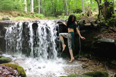 Esmer kadın dağ şelalesinin yanında poz veriyor, Karpatya ormanı, yaz tatili.