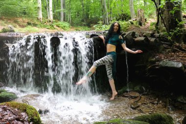 Esmer kadın dağ şelalesinin yanında poz veriyor, Karpatya ormanı, yaz tatili.