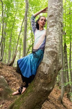Yazın Ukrayna 'da Kayın Karpat Ormanı' ndaki bir ağacın yanında boho elbiseli esmer bir kadın.
