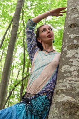Yazın Ukrayna 'da Kayın Karpat Ormanı' ndaki bir ağacın yanında boho elbiseli esmer bir kadın.
