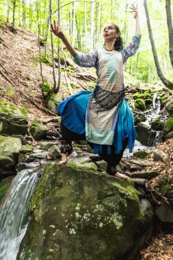 Mavi elbiseli esmer kadın bir dağ deresinin yanında duruyor, Ukrain.