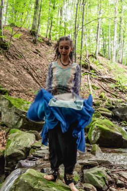 Dere kenarında dans eden esmer kadın, mavi kıyafetler, yaz, Karpatyalı.