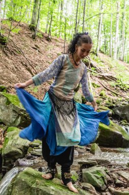 Dere kenarında dans eden esmer kadın, mavi kıyafetler, yaz, Karpatyalı.