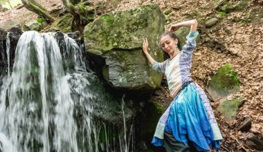 Mavi elbiseli esmer kadın şelalenin yanında dans ediyor, yaz, karpatyalı.