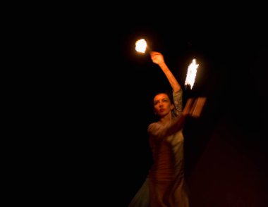 young woman doing fire show at night, motion blur of flam