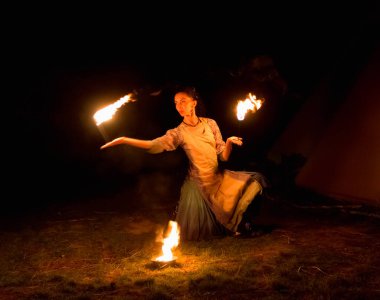 young woman doing fire show at night, motion blur of flam