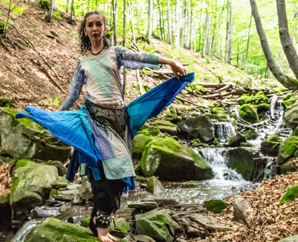 Dere kenarında dans eden esmer kadın, mavi kıyafetler, yaz, Karpatyalı.