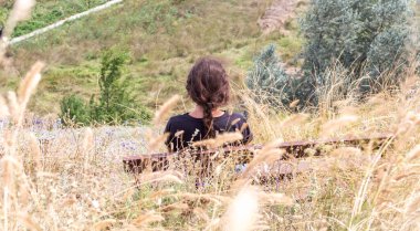 Kız bir uçurumun yamacında oturuyor ve denize bakıyor, dinleniyor, yaz, siyah