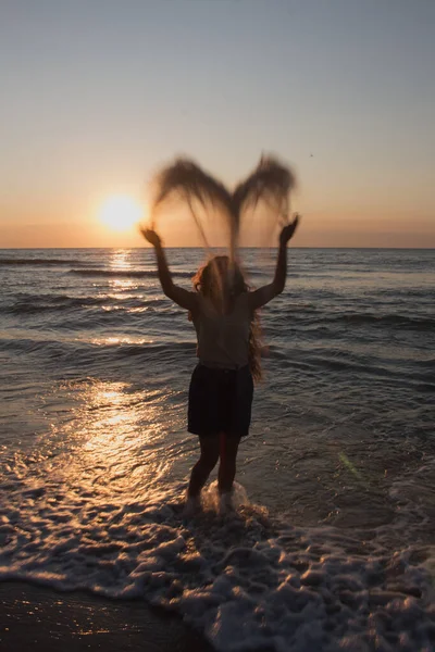 girl throws sand on the seashore, sunset on the beach, summe