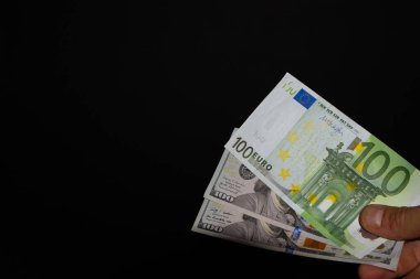 İki adet 100 Dolarlık banknot ve 100 Avroluk banknot, siyah arka planda, 100 Dolarlık banknot elle transfer ediliyor.