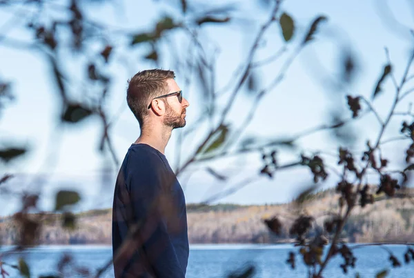 Young man staring at the distance seen through tree branches