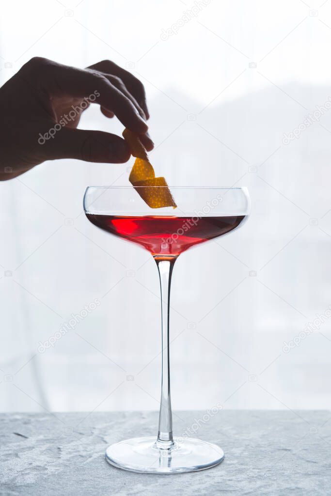 Dropping a lemon twist in a red cocktail 