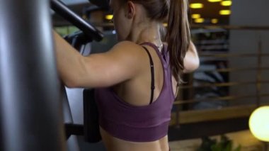 Kız vücut geliştirme insanı, genç ekipman dayanıklılığı ve simülatör egzersiz formundaki fitness salıncağıyla meşgul. Motosikletli kadınlar çekici, ince bisiklet makineleri