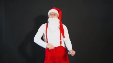 Noel Baba sarı yemek stili, askılar Noel tatili kostümü. Sakallı olgun, zaman siyah bir arka planda neşeyle dans ediyor.
