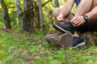 Parkta bağcıklarını bağlayan bir adam ormanda, meşe ağaçları yeşil çimenler genç sporcu. Spor koşusu, yaşam tarzı açık hava bacak maratonu, ağaç adam. Yaz vücudu çapraz