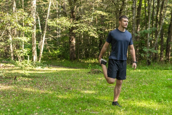 屋外の公園では、森の周り、オークの木の緑の草の若い永続的な運動選手のスポーツワークアウトジョガーウェルネスジョギング男を実行します。大人のエネルギーのクロス、ストレッチ ストックフォト