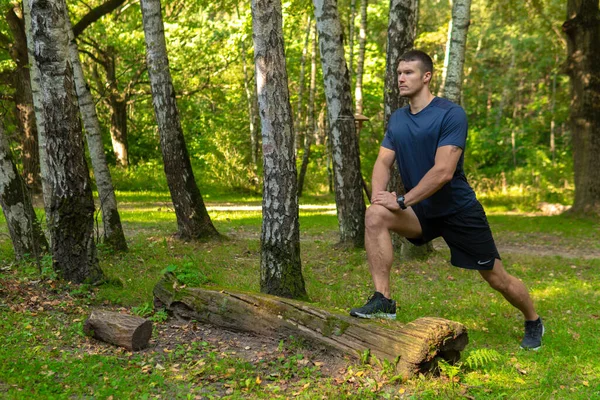 Dayanıklı genç bir atlet ormanda, açık havada, ormanın etrafında, ağaçlarda esneme hareketleri yapıyor. Aktif orman, açık havada antrenman maratonu, ağaçların refahı. Yetişkin vücudu çalışıyor