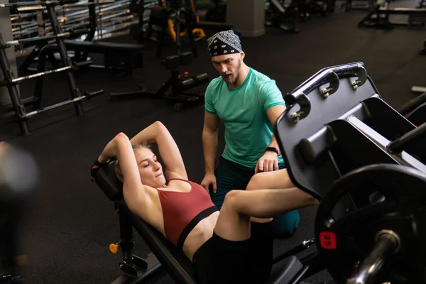 Eğitmen, güzel bir müşteriye spor salonunda spor yapma kavramını öğreterek öğleden sonraları modern spor yapma konusunda yardımcı olur.