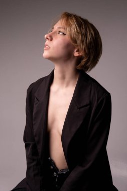 Sarışın bir kız, açık göğüslü, açık göğüslü beyaz bir kadından sağlıklı ve taze bir model portresi için çıplak siyah bir geçmişle oturuyor. Seksi stüdyo mayosu, beyaz.