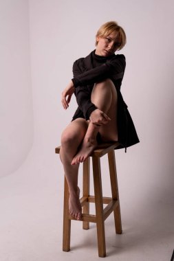 Bir sandalyede oturan kız, elini sallayarak bacağına sarıldı. Yetişkin, çekici arka plan güzellik göğüslerini sağlıklı, saf ve şehvetli bir vücut figüründen ayırdı. Cilt spa mayosu,