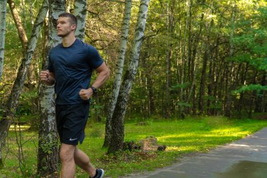 Atletin biri parkta koşuyor, ormanın etrafında, meşe ağaçları yeşil çimenler genç dayanıklı atlet koşucu tabiatı, fitness koşucusu ağaçlara uygun yetişkin mesafesi uzanıyor.