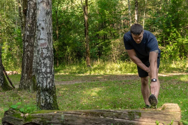 Een jonge, duurzame atleet rekt zich uit in het bos, rond het bos, eikenbomen. sport oefening, training jong wellness mannetje, park leisure cross, hardlopers strekt zich uit — Stockfoto