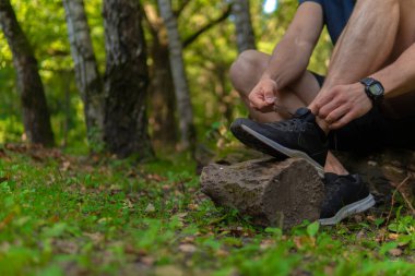 Parkta bağcıklarını bağlayan bir adam ormanda, meşe ağaçları yeşil çimenler genç sporcu. Koşu sporu sporu sağlık maratonu, park eğlence baharı, esneme.