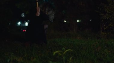 Elinde çekiçle parkta yürüyen ürkütücü bir kadın.