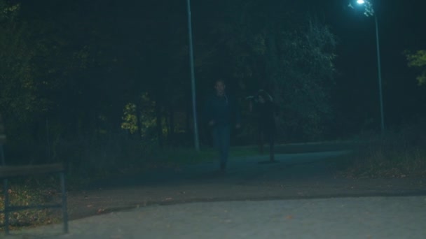 Tipo huyendo de una mujer espeluznante con un martillo en un parque nocturno — Vídeos de Stock