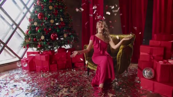Красива щаслива брюнетка в червоній вечірній сукні. жінка сміється, розкидаючи блискучий святковий папір. знаменитостей. Різдвяні та новорічні подарунки від чарівників та дерево в готелі . — стокове відео