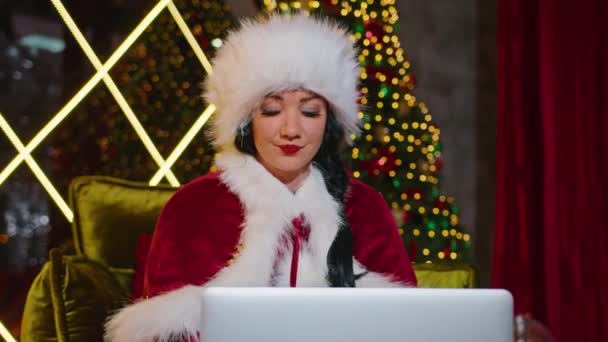 Lykkelig kvinde Mrs. Santa kommunikerer på laptop i hendes julekontor. ferie i karantæne. fjernkommunikation, feriegaver og rabatter. – Stock-video